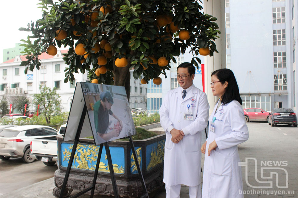 Vợ chồng bác sĩ CKII Nguyễn Thị Thu Minh bên bức ảnh do chính anh Hoàng chụp được trưng bày tại khuôn viên Bệnh viện nhân kỷ niệm 70 năm Ngày thầy thuốc Việt Nam.