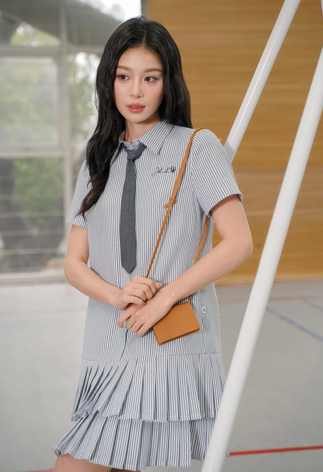Gam màu xám nhạt xen kẽ sọc trắng giúp thiết kế đầm sơ mi xếp ly có hai tầng váy bồng bềnh lãng mạn cưa đổ trái tim của chị em. Với phom dáng trang phục suông rộng, quý cô có thể biến hóa hình ảnh nhanh chóng và dễ dàng
