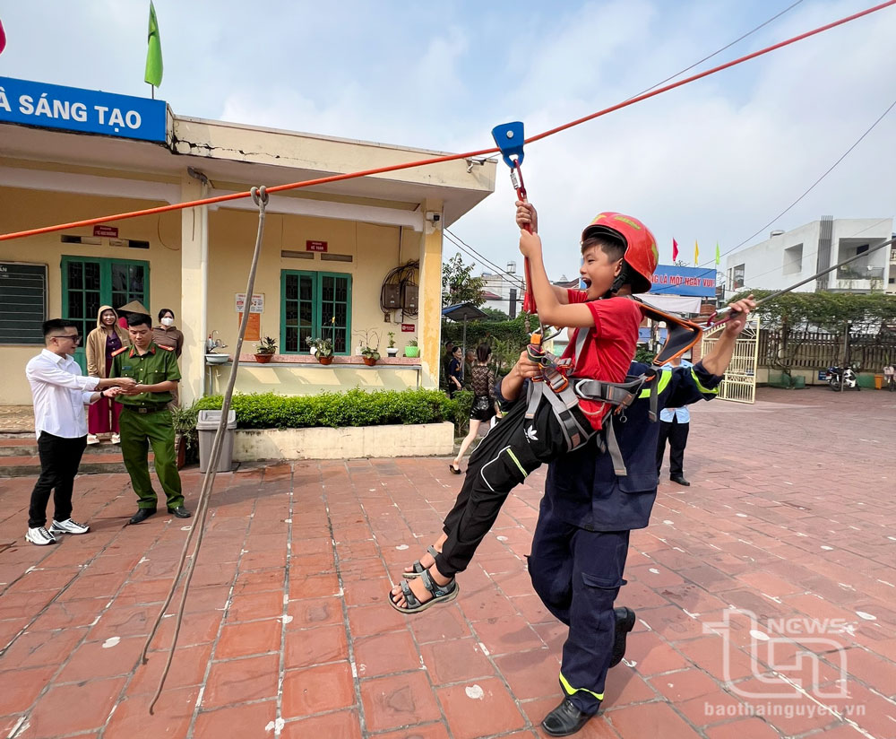 Cán bộ, chiến sĩ công an hướng dẫn, hỗ trợ học sinh Trường Tiểu học Nguyễn Huệ (TP. Thái Nguyên) thực hành, trải nghiệm thoát nạn bằng dây thả chậm.